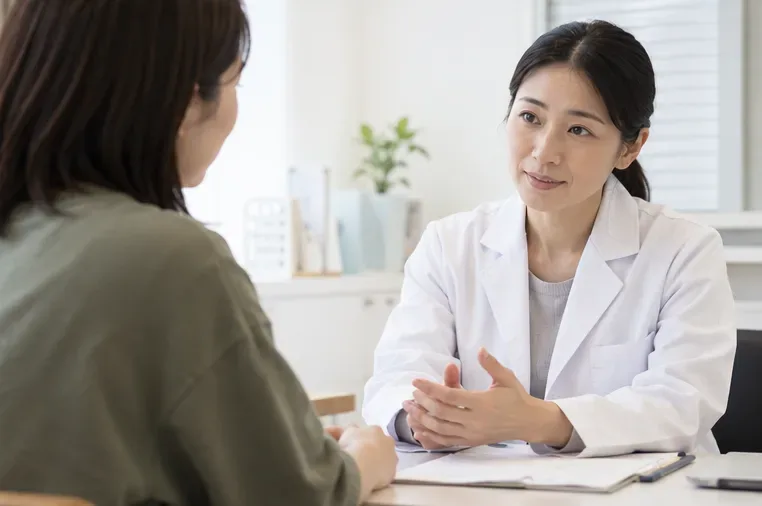 診察室で女性が医療者と向かい合い、机越しに話している。